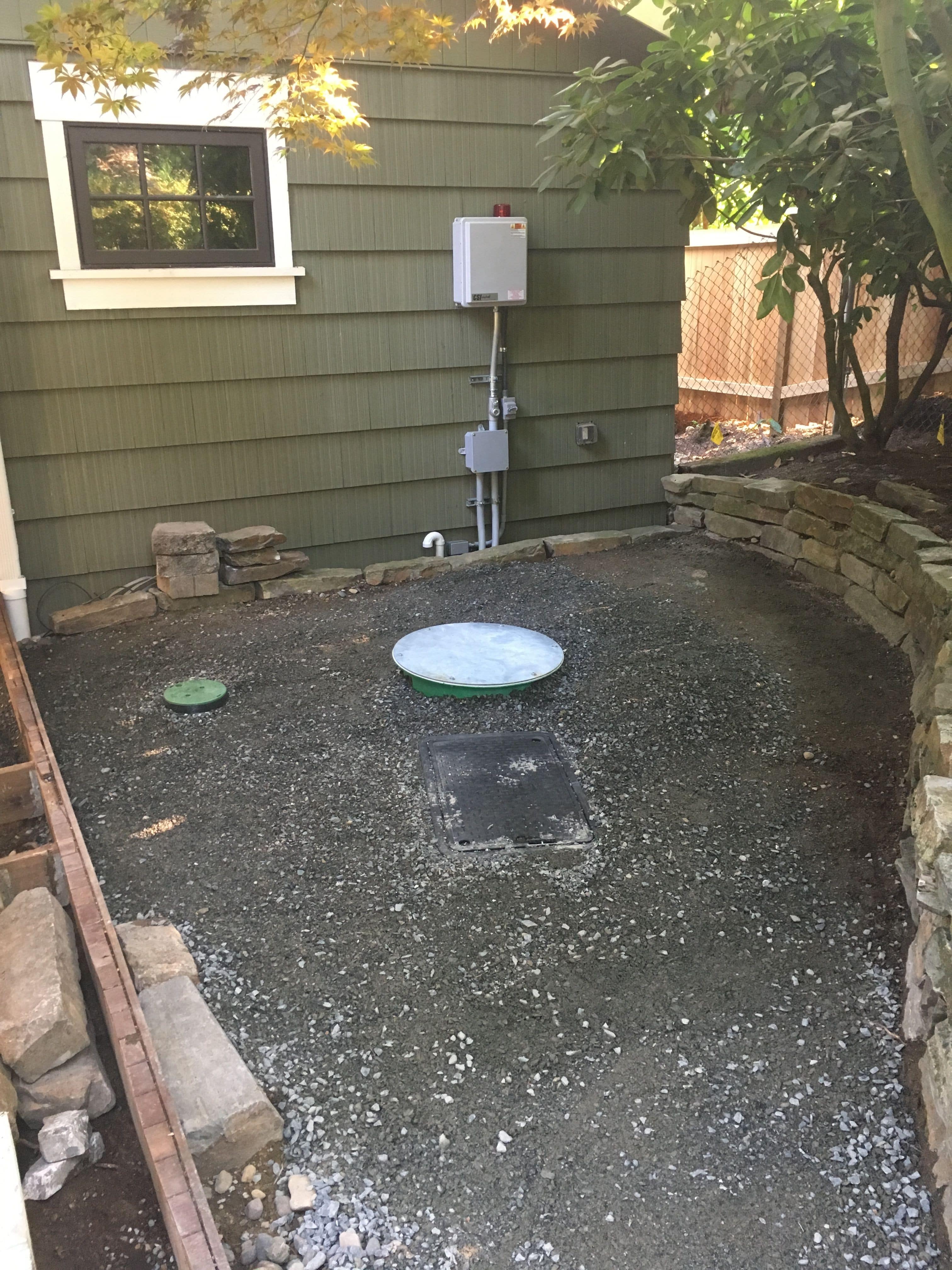 A 24" round top of sewer tank installed next to a rectangle plastic box housing the clean out for the pressure pump line and within a few feet of the house.